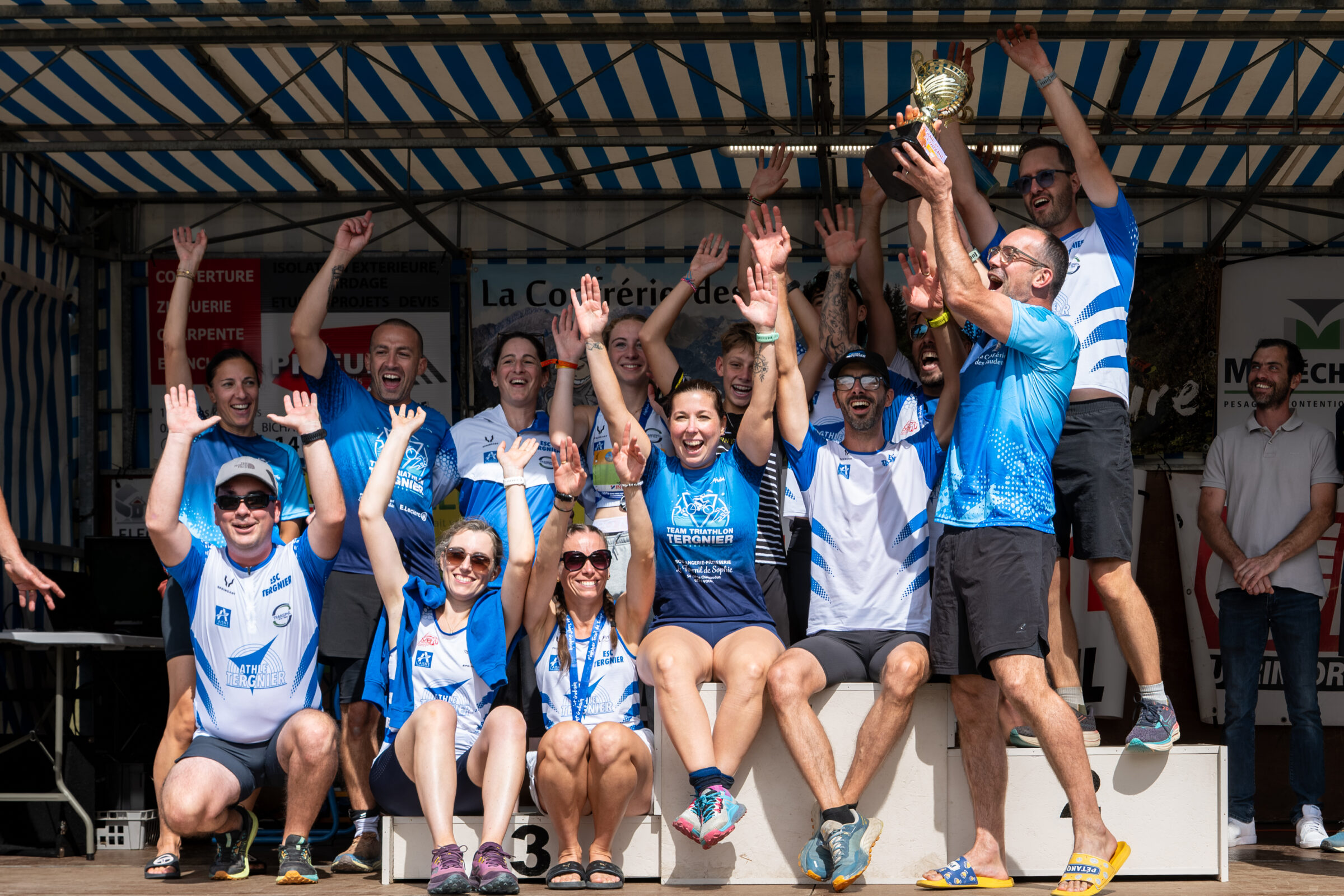 Un groupe de participants se retrouve sur la scène des récompenses, coupe levée au-dessus des coureurs.